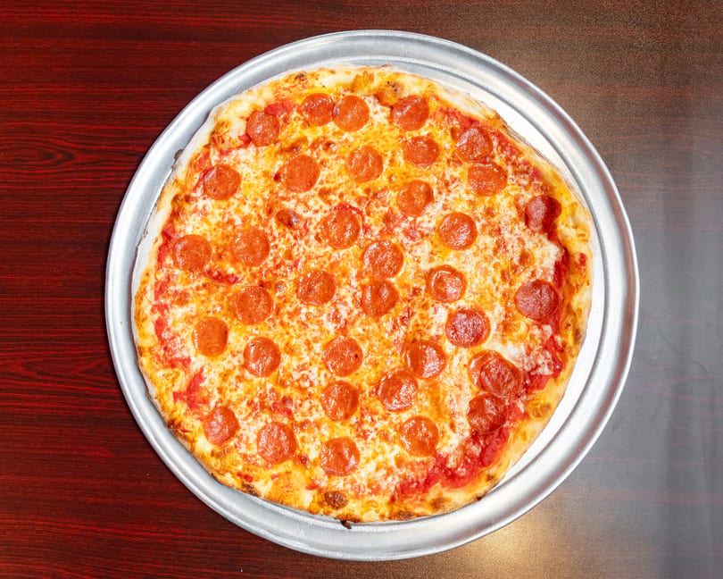 A whole pepperoni pizza with melted cheese and tomato sauce on a metal tray.