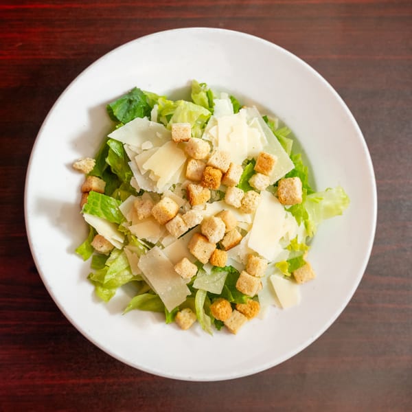 Overhead view of a Caesar salad with romaine lettuce, croutons, and shaved Parmesan cheese.