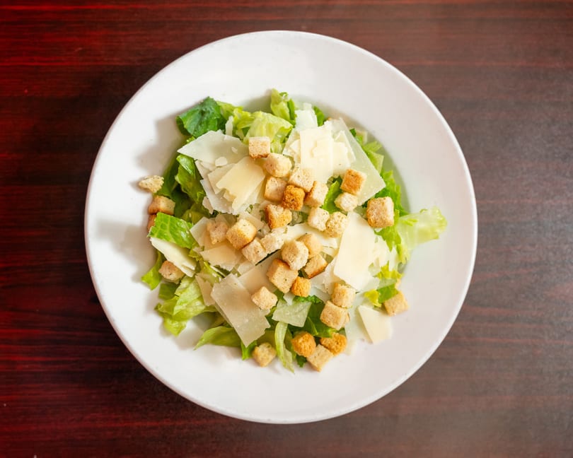 Overhead view of a Caesar salad with romaine lettuce, croutons, and shaved Parmesan cheese.
