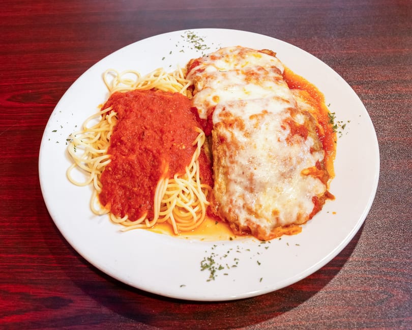 Chicken parmesan with melted cheese and spaghetti with red sauce on a white plate.