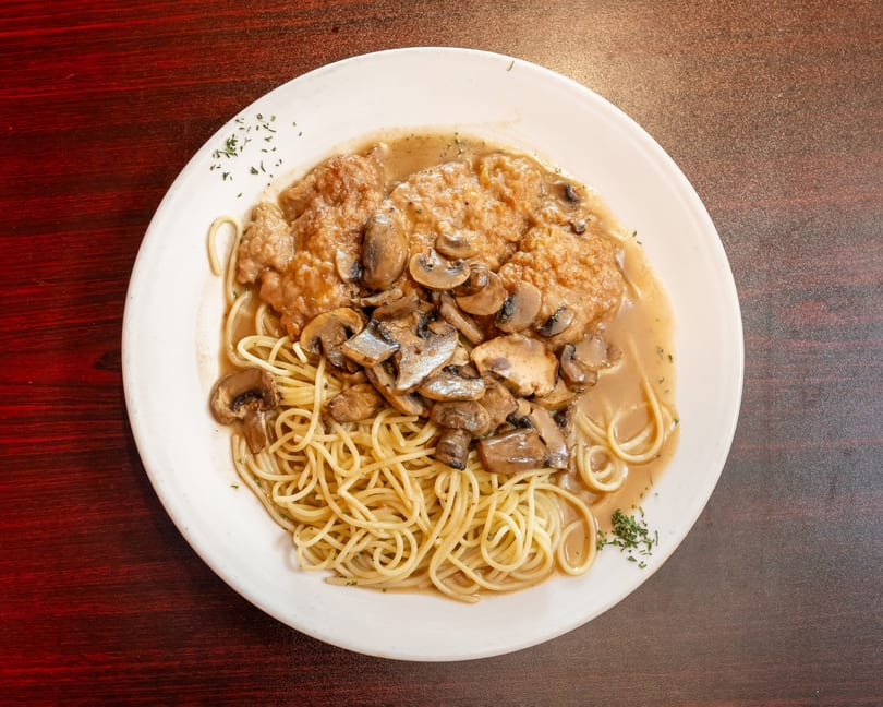 Chicken Marsala with mushrooms and spaghetti on a white plate, viewed from above.