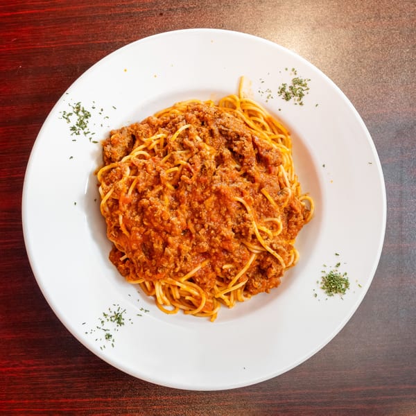 A white plate filled with spaghetti and a rich, red meat sauce, garnished with parsley.