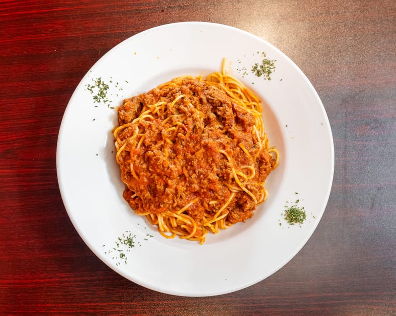 A white plate filled with spaghetti and a rich, red meat sauce, garnished with parsley.