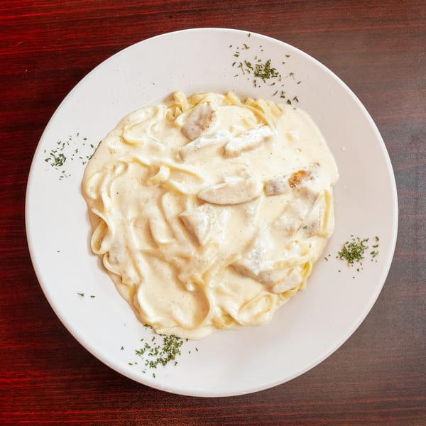 Creamy chicken alfredo pasta with parsley flakes on a white plate, on a dark wooden table.
