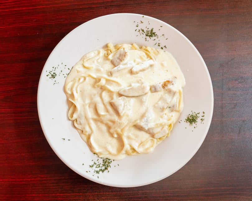 Creamy chicken alfredo pasta with parsley flakes on a white plate, on a dark wooden table.
