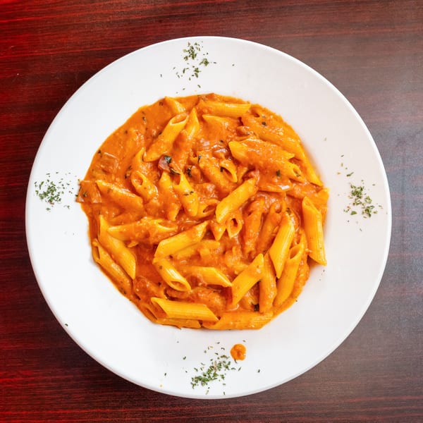 A white plate filled with penne pasta in a creamy orange sauce, garnished with herbs.