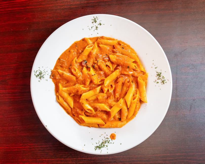 A white plate filled with penne pasta in a creamy orange sauce, garnished with herbs.