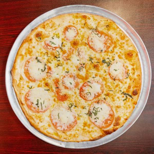 A whole Margherita pizza with fresh mozzarella, sliced tomatoes, and basil on a metal tray.