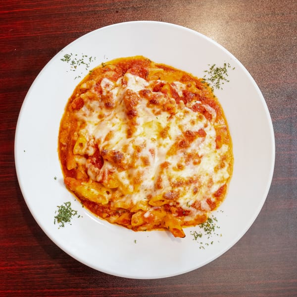 Baked penne pasta with melted cheese and tomato sauce, garnished with herbs on a white plate.
