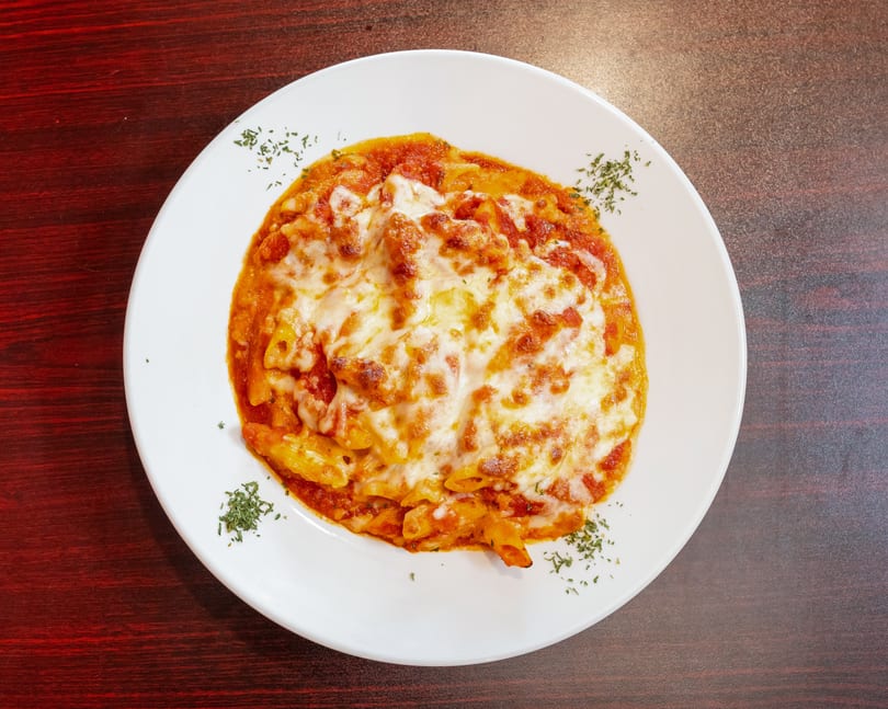 Baked penne pasta with melted cheese and tomato sauce, garnished with herbs on a white plate.