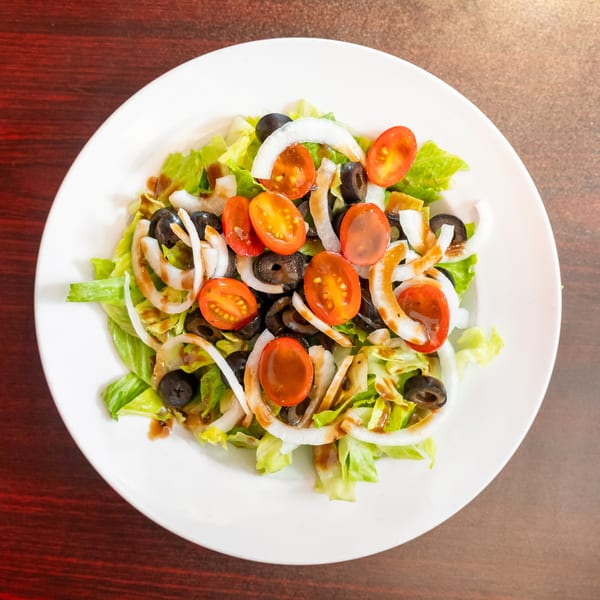 A fresh garden salad with lettuce, tomatoes, black olives, and onion rings on a white plate.