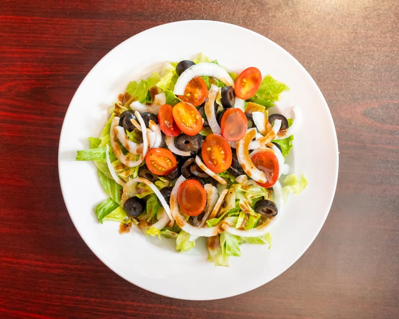 A fresh garden salad with lettuce, tomatoes, black olives, and onion rings on a white plate.